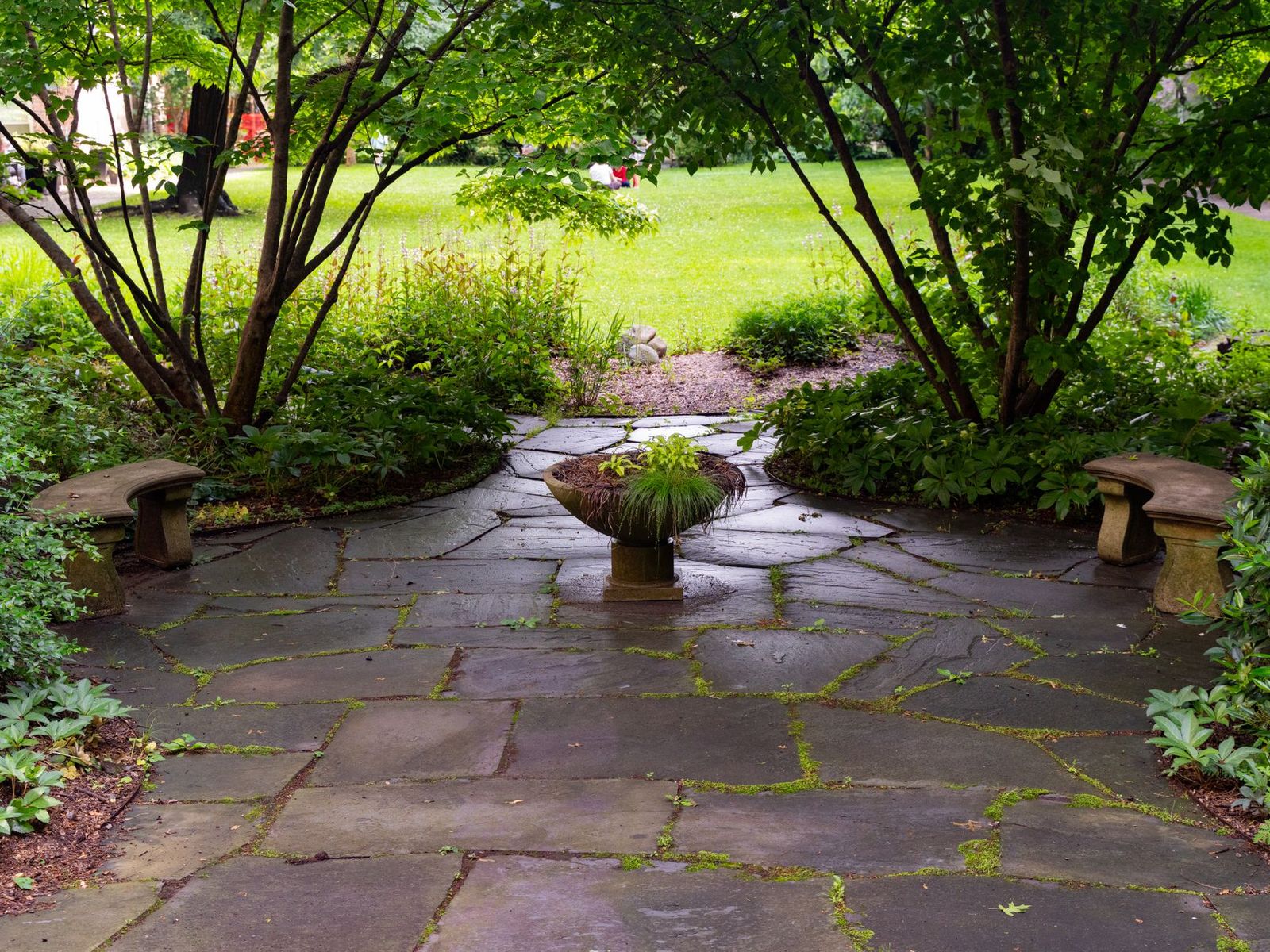 Flagstone patio surrounded by mature trees and garden beds